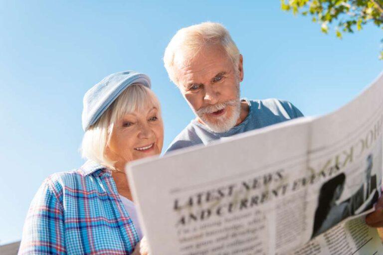 Elderly couple feeling excited while reading morning local news outside house